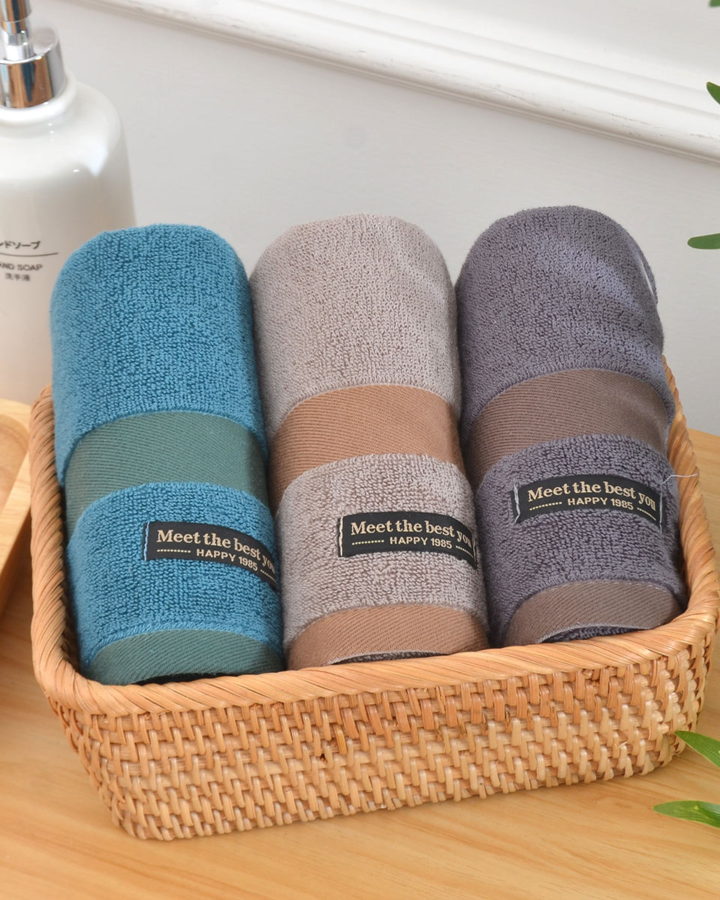 Trois serviettes de bain roulées bleu, beige et gris dans un panier